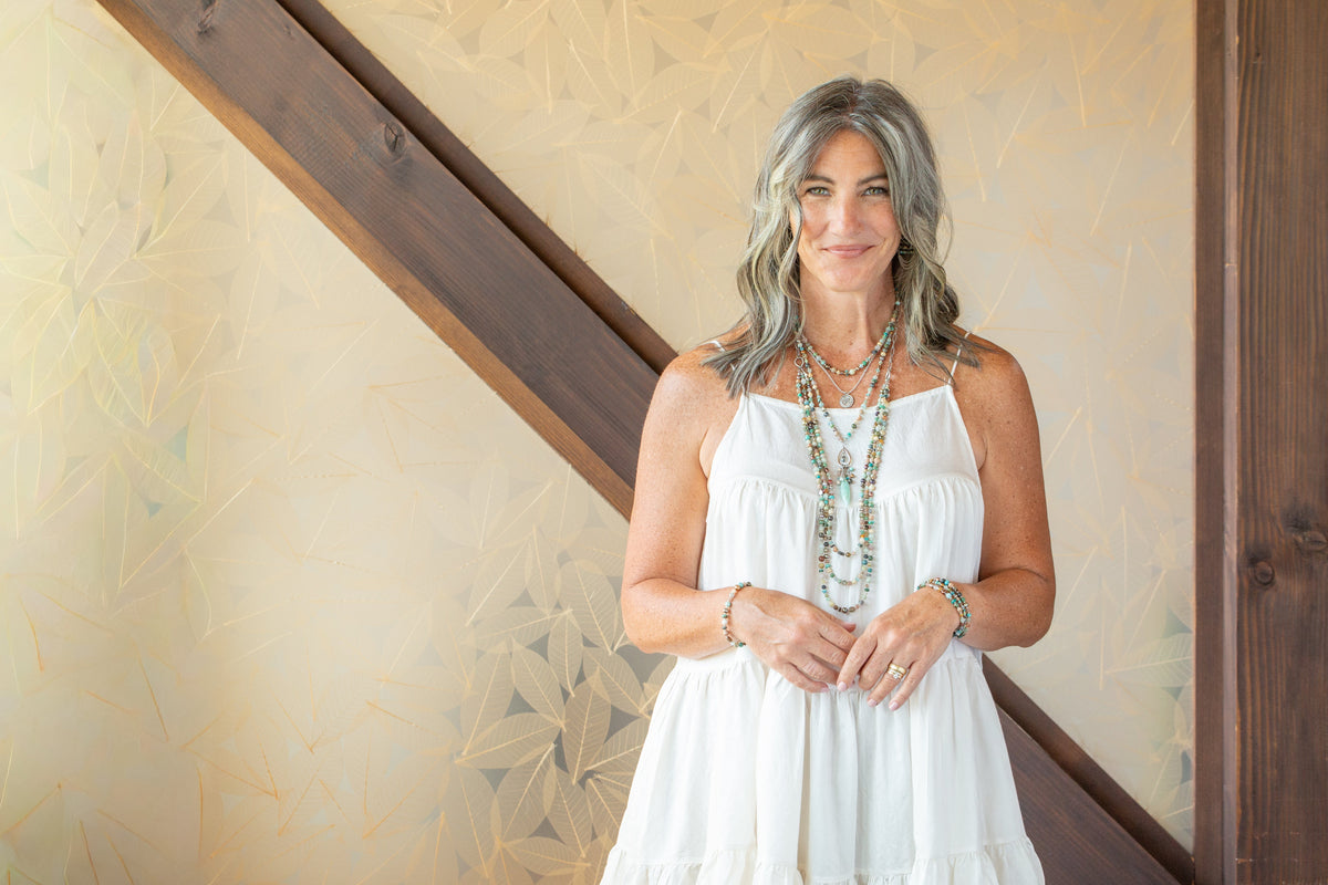 Model wearing layered handcrafted turquoise, amazonite, and labradorite gemstone necklaces with a white sundress in a studio setting.